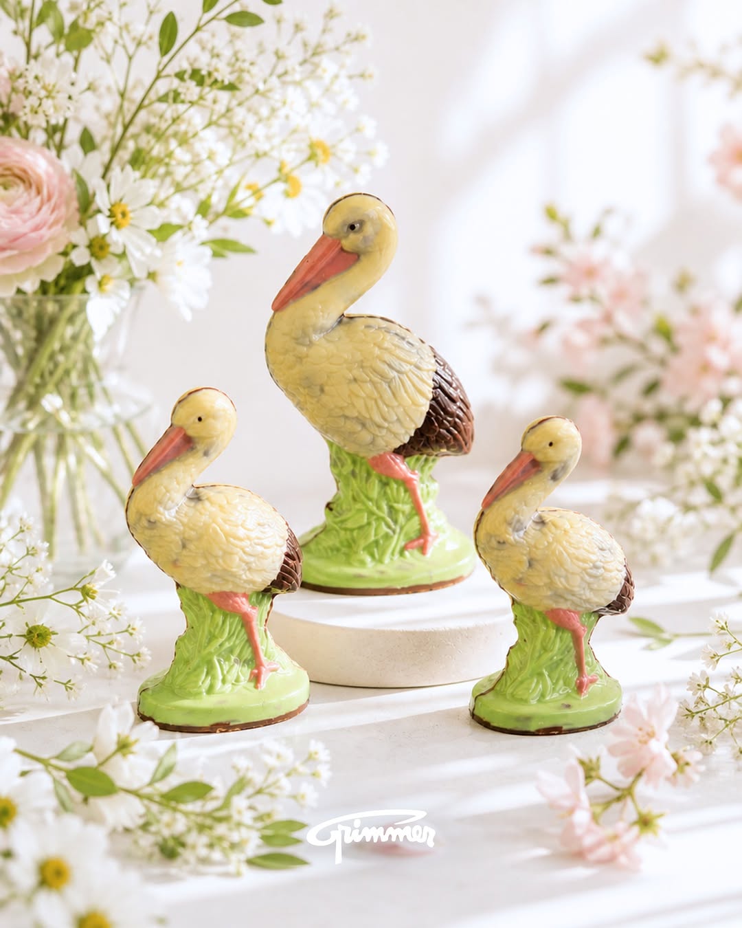 Trois cigognes en chocolat de la Maison Grimmer, entourées de fleurs